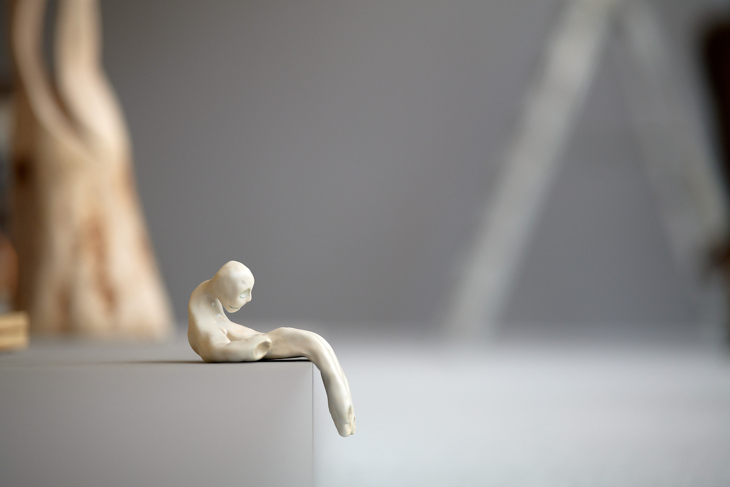 Fotografi på en vit lerskultptur föreställande en sittande figur. Figuren har ett mäsnkligt huvud och en kropp i form av en hand.